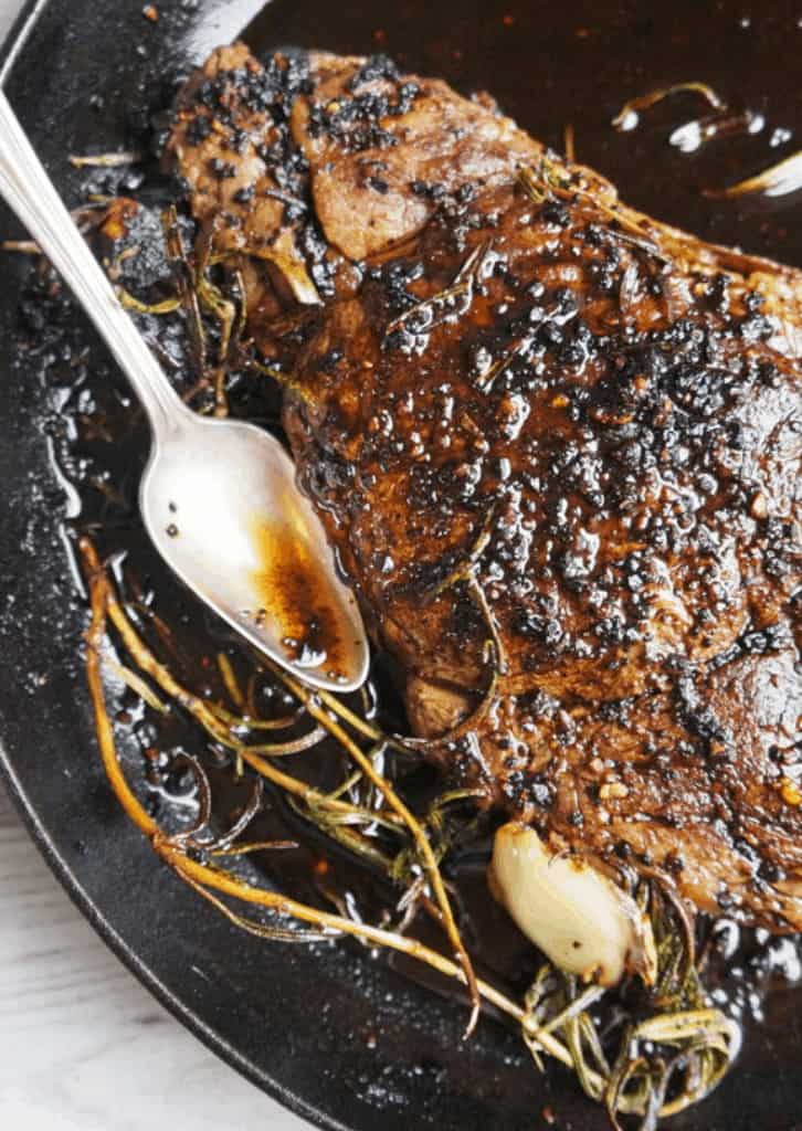 ribeye steak in a cast iron skillet with a silver spoon