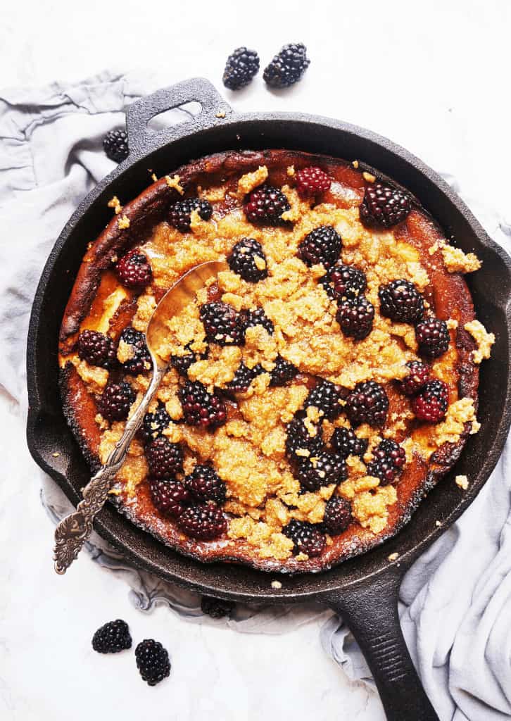 overhead shot of Keto Dutch Baby with Blackberry Crumble in a skillet with a spoon