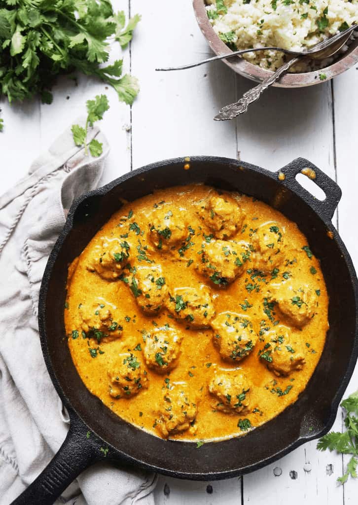 keto butter chicken meatballs in a cast iron skillet with cauliflower rice