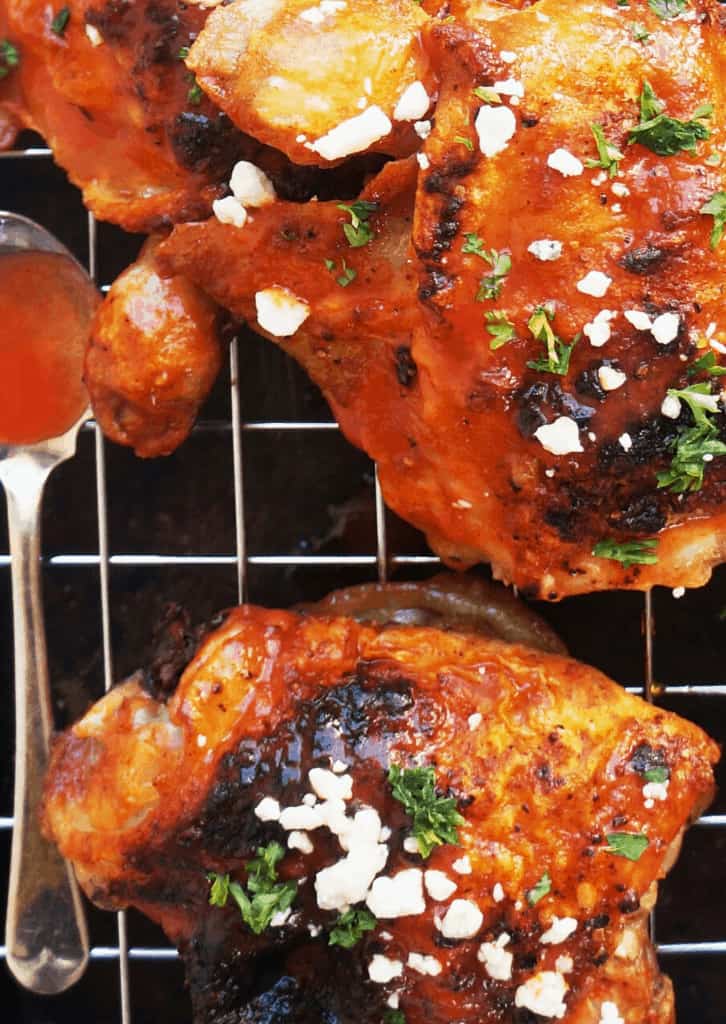 baked chicken thighs with spoonful of buffalo sauce on wire rack