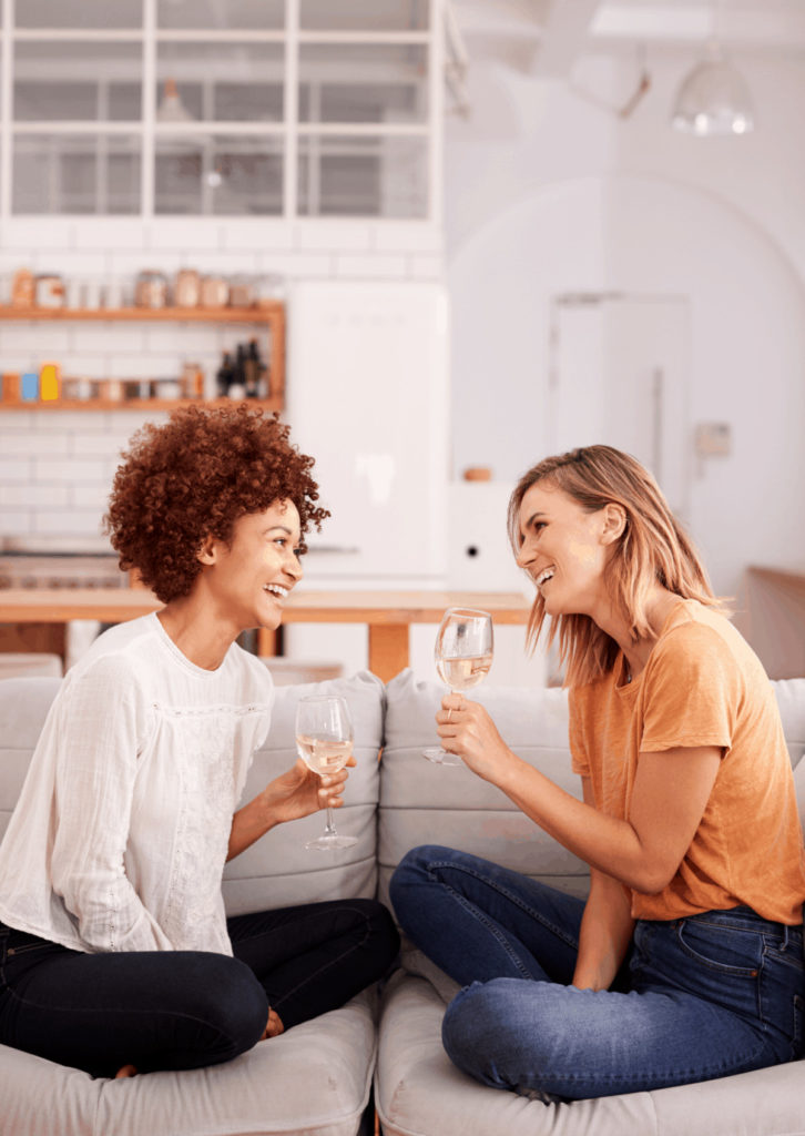 two women drinking white wine on a couch