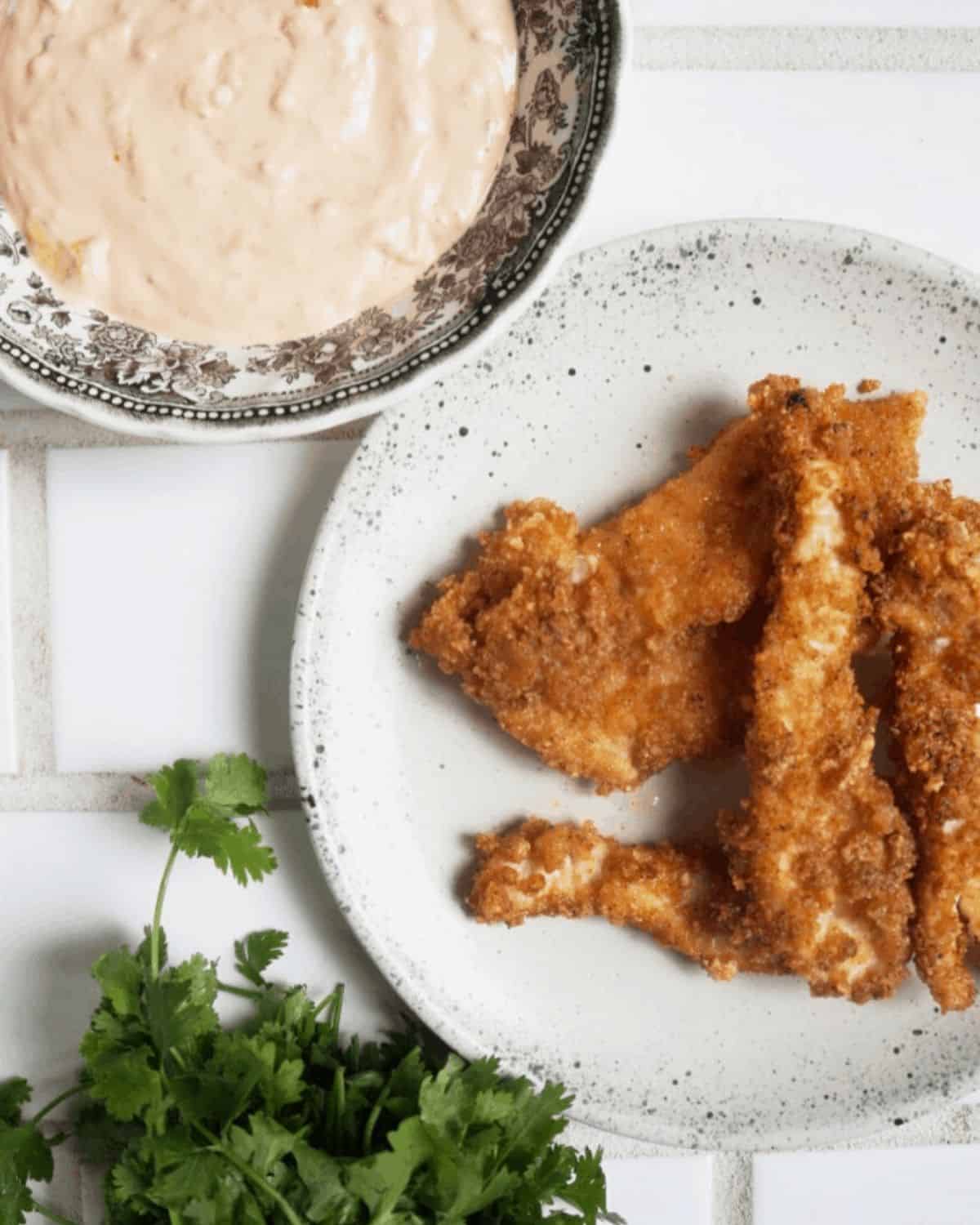 Keto bang bang sauce in a bowl next to a plate of chicken fingers.