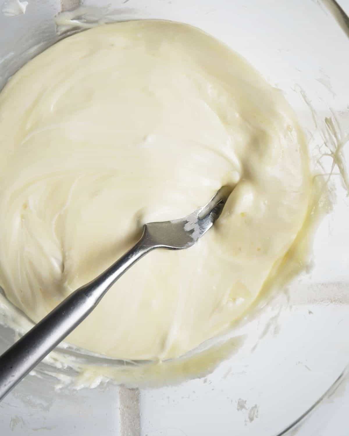  Mozzarella fondue et fromage à la crème dans un bol en verre avec une fourchette en remuant.