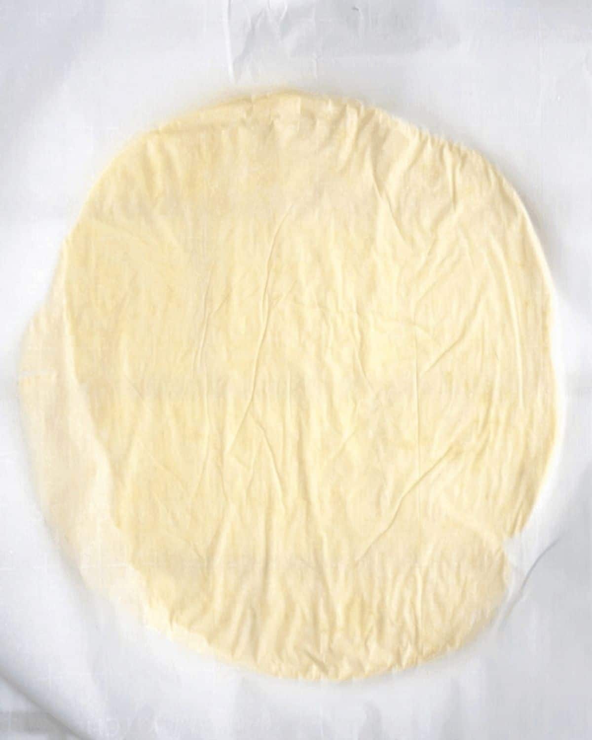  La pâte roulée en un cercle de 8 pouces de large entre deux morceaux de papier sulfurisé.