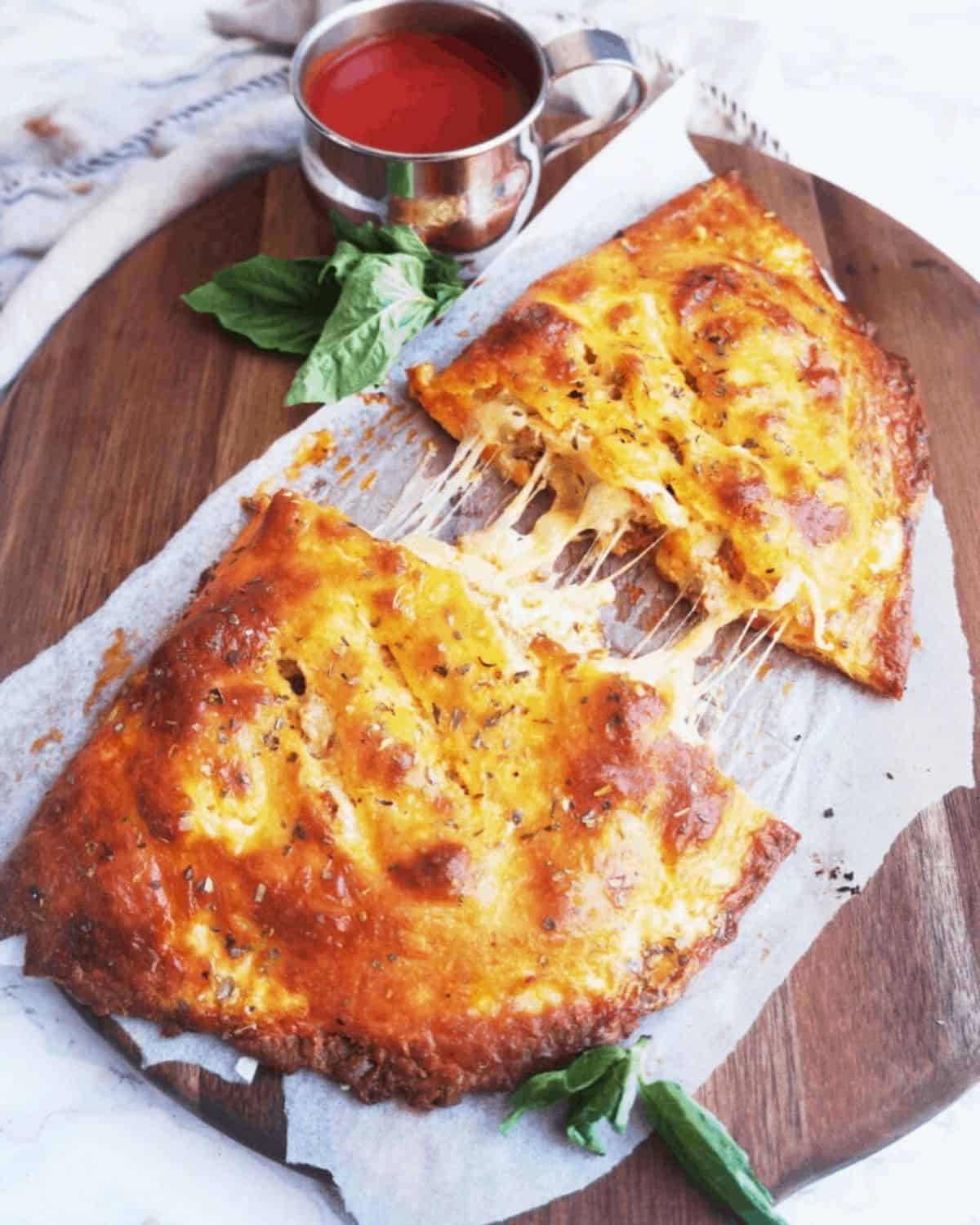 Finished keto calzone cut in half served on a wooden cutting board with a basil garnish.