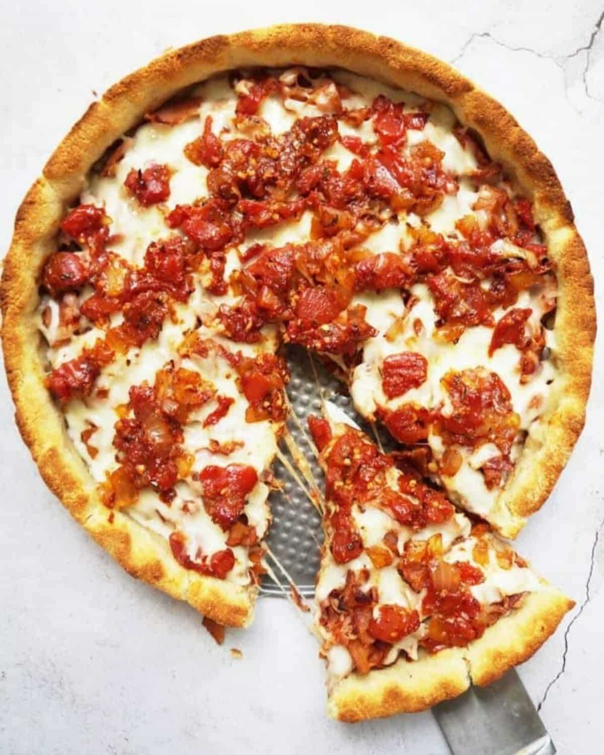 Overhead shot if the baked deep dish pizza with a slice being pulled away from the rest of the pie on a spatula.