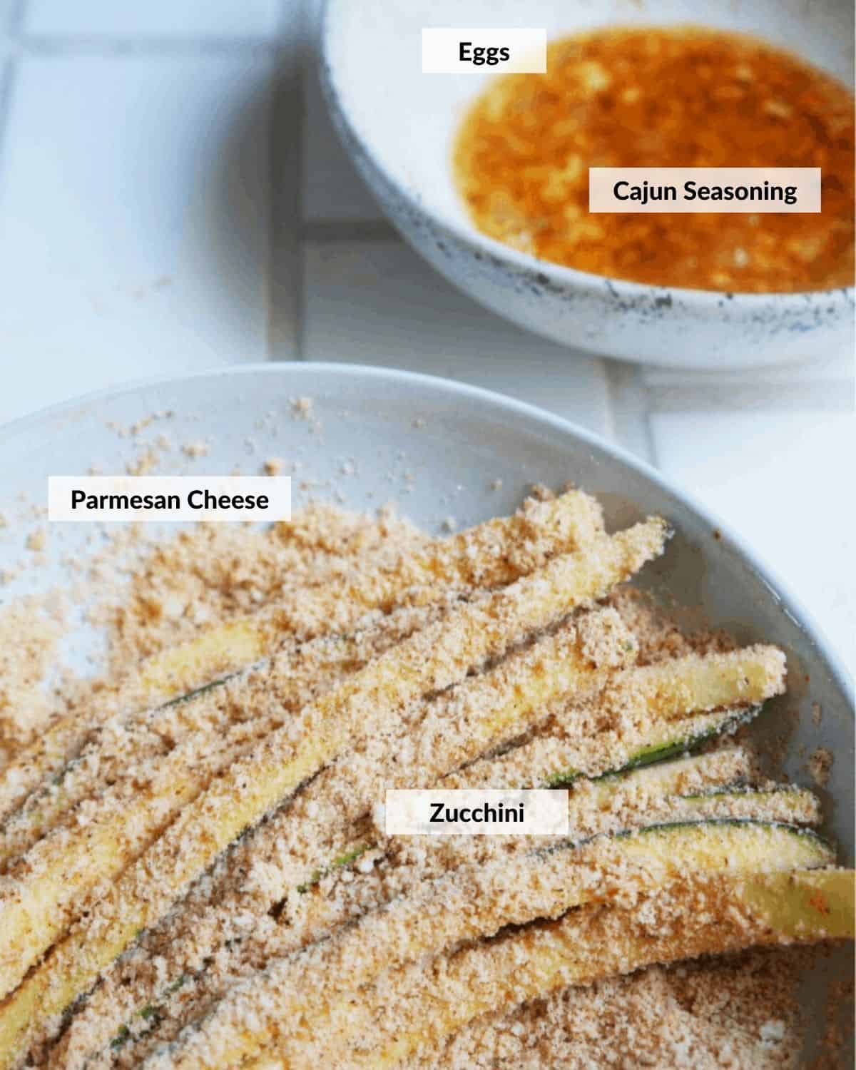 Zucchini strips covered in Parmesan cheese on a plate with a bowl of beaten eggs and Cajun seasoning.