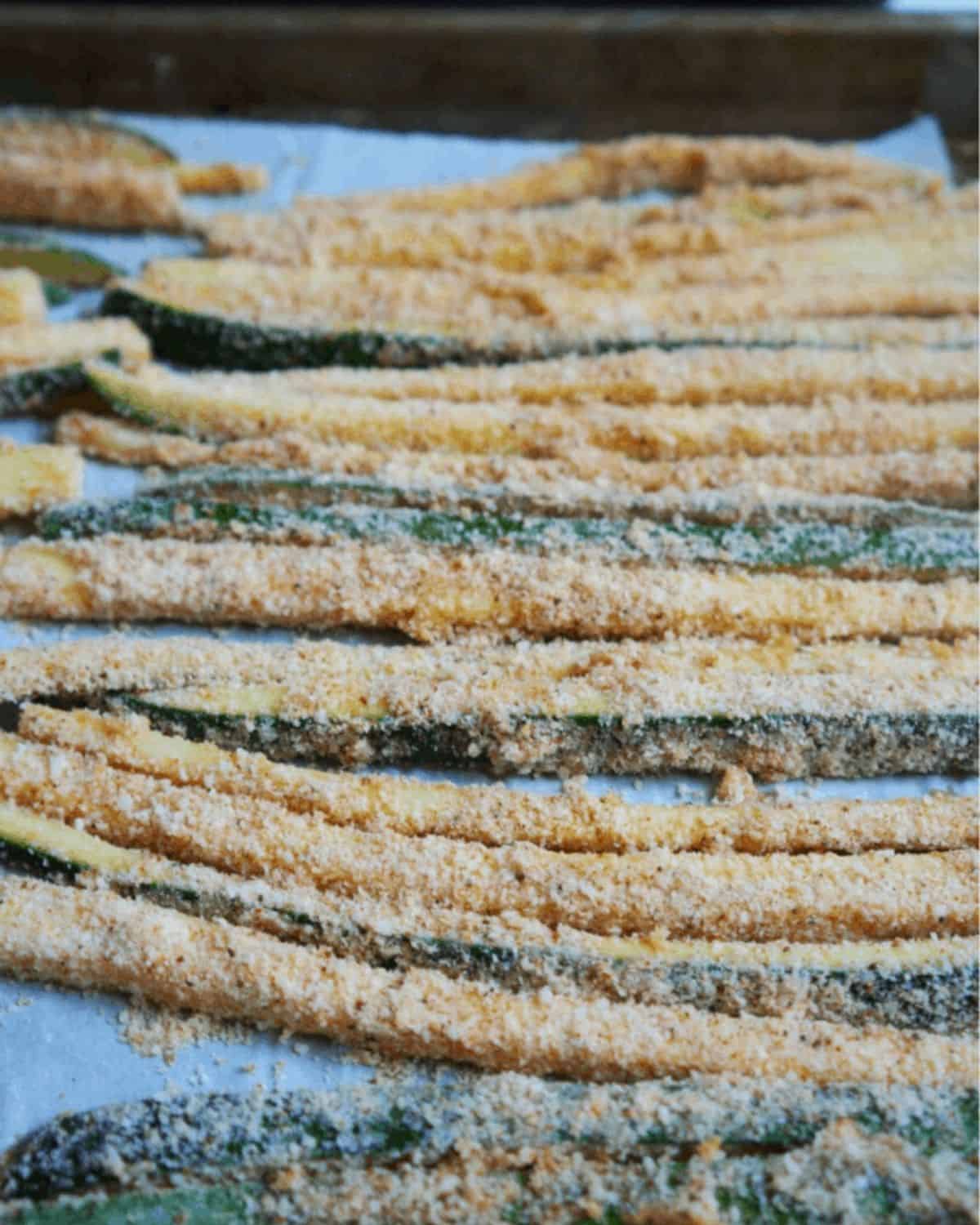 Side shot of the uncooked fries that are coated in parmesan cheese arranged on a baking sheet.