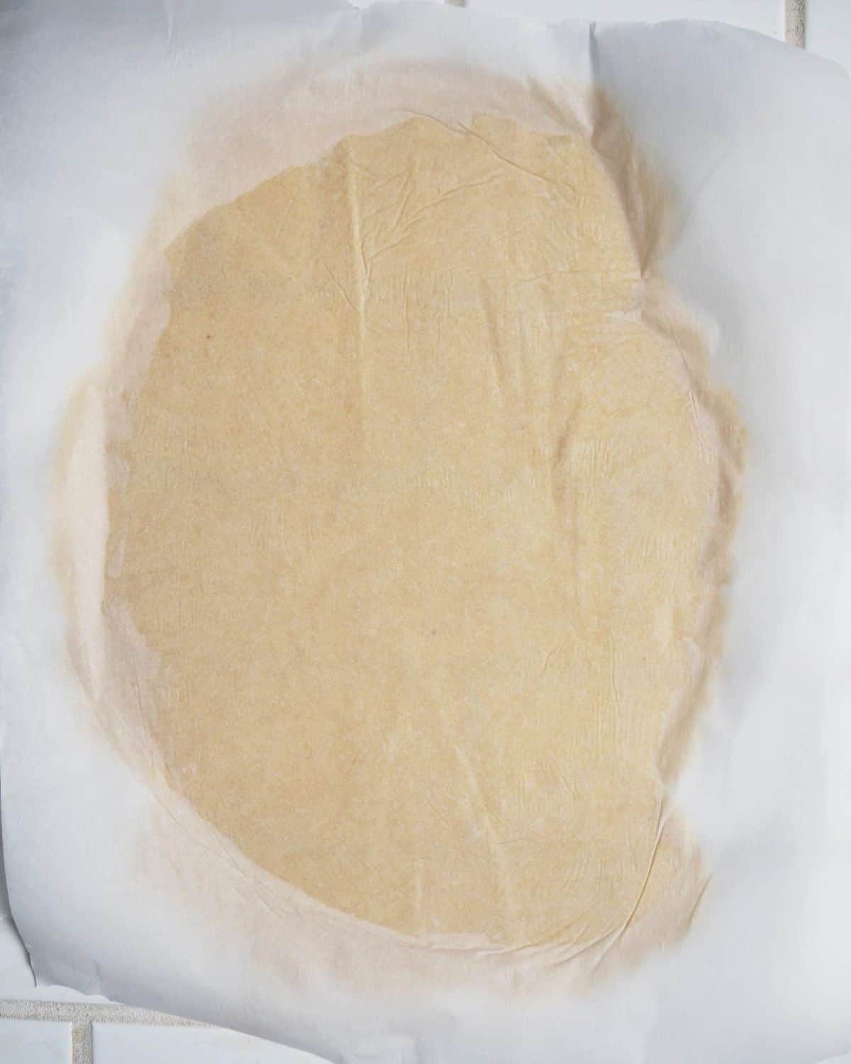 The wonton dough rolled out into a large oval between two pieces of parchment paper.
