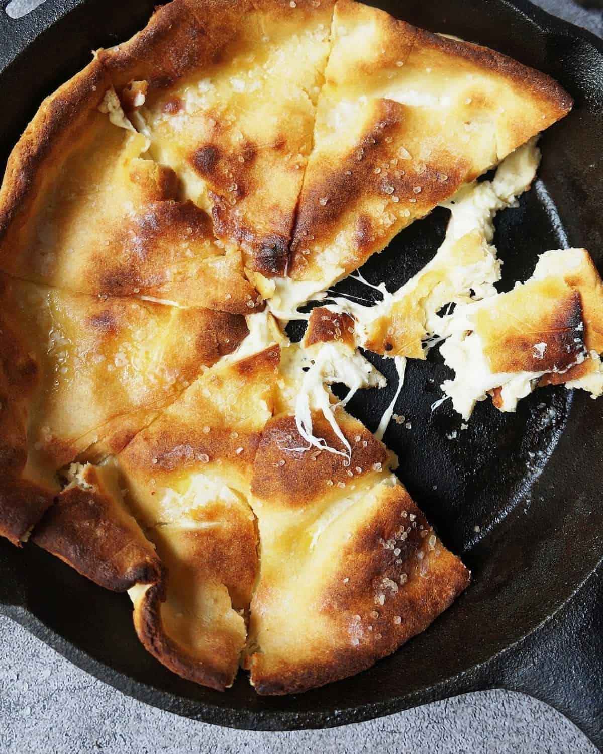 Italian bread in cast iron skillet with one slice pulled apart exposing the cheese