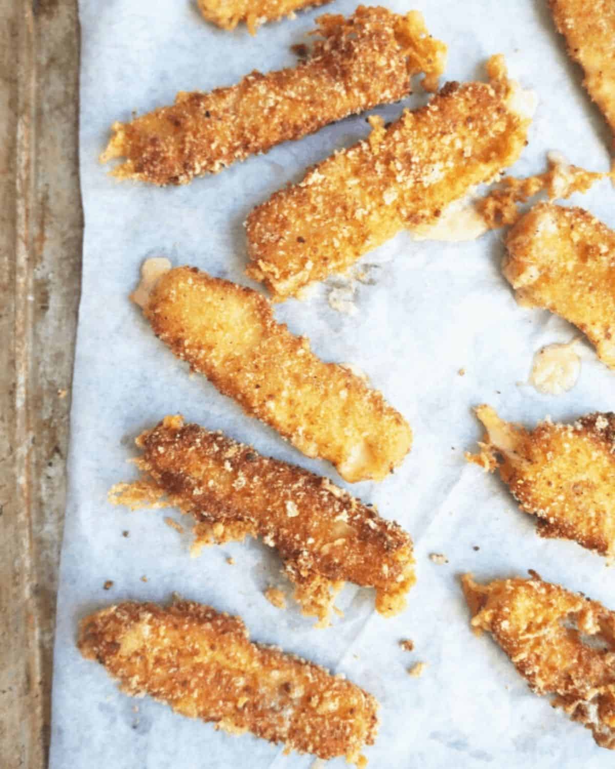 Freshly fried cheese sticks cooling in a single layer on parchment paper