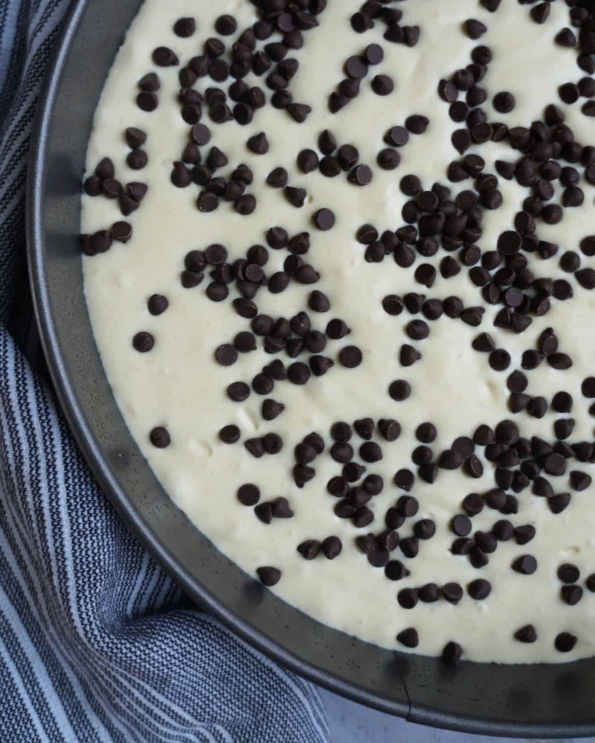keto cheesecake filling in a pan before baking with chocolate chips sprinkled over top