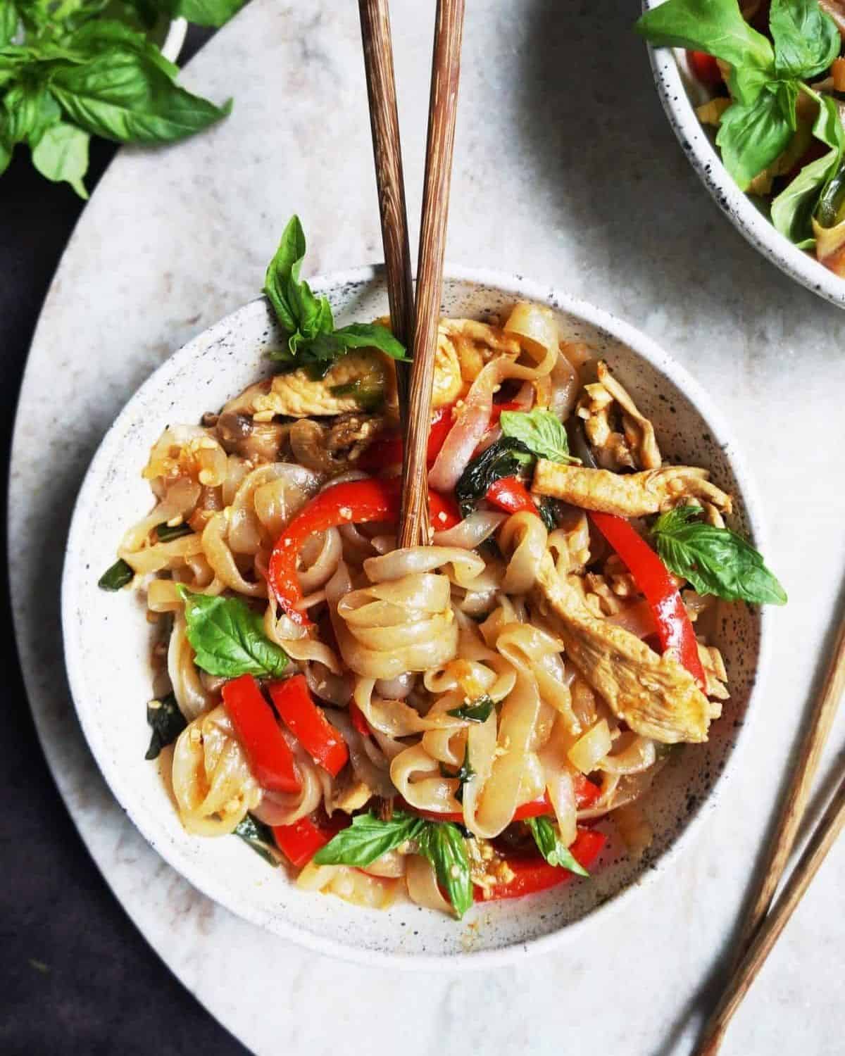 Overhead shot of Thai drunken noodles in a white bowl with chopsticks criss crossed in the bowl