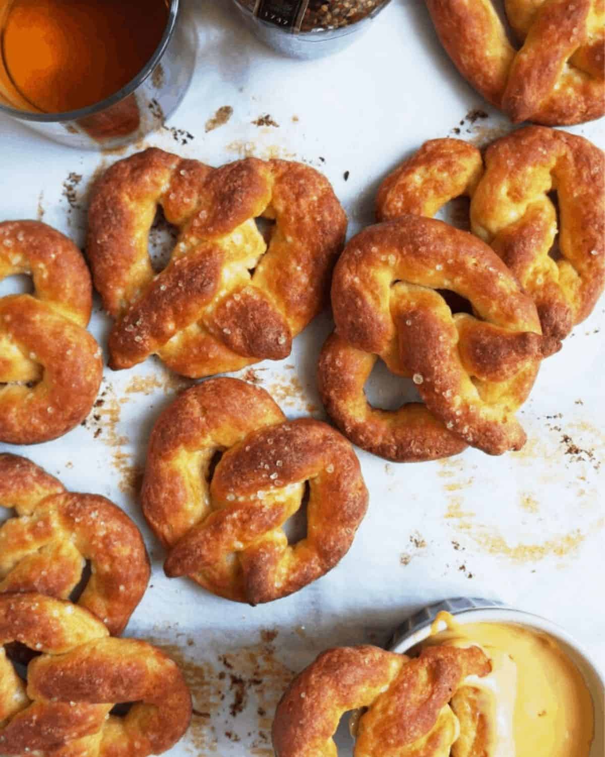 seven baked pretzels on white parchment paper next to a container of cheese dip