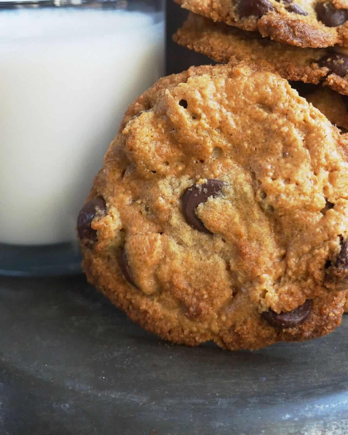 close up of baked cookie next to a cup of milk